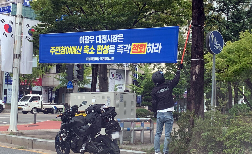 더불어민주당 대전시당이 게시한 '이장우 시장 비판 현수막'을 누군가 잘라내고 있다. 제보사진.